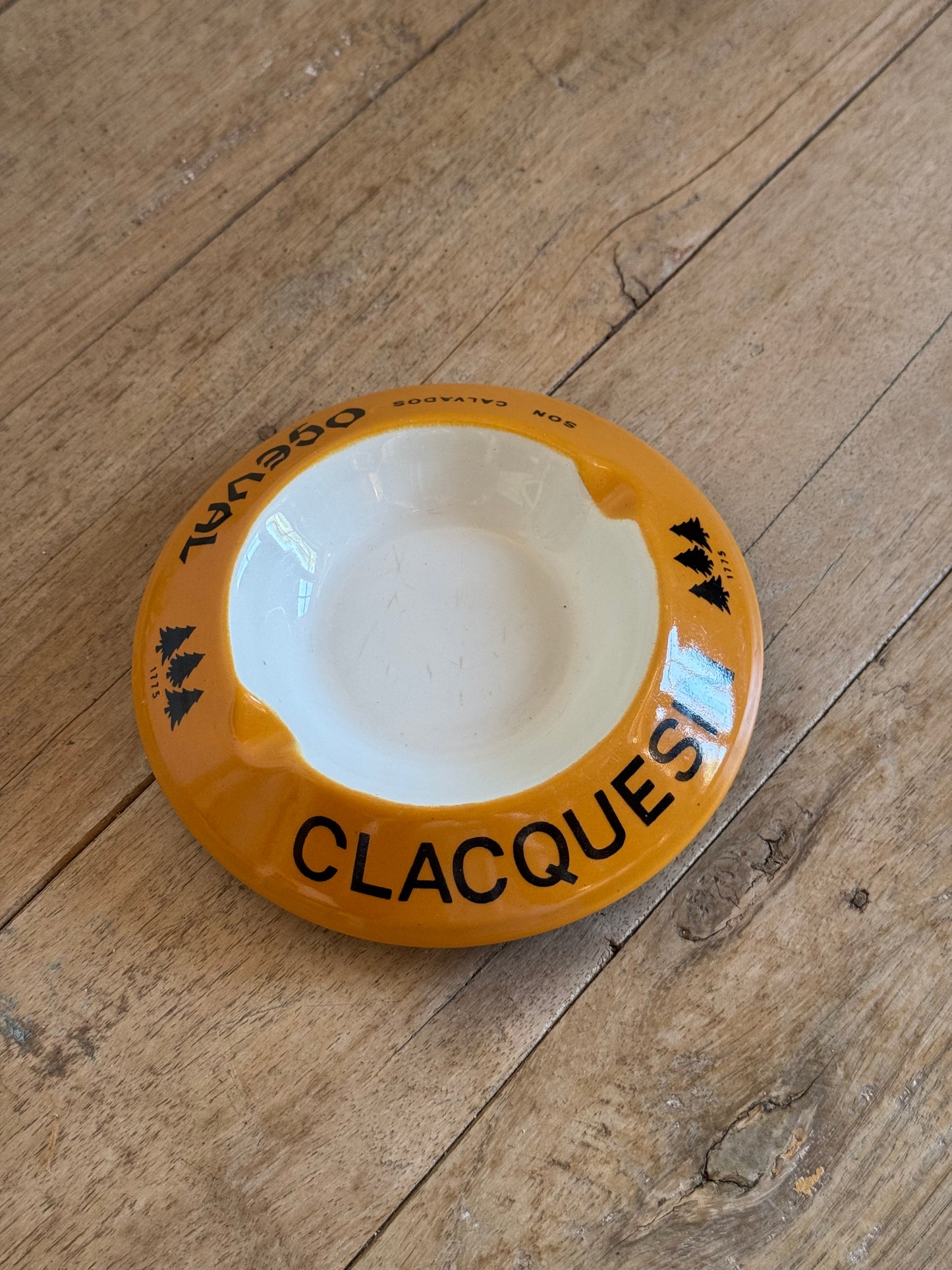 Round ceramic ashtray with 'Clacques' branding on a wooden surface