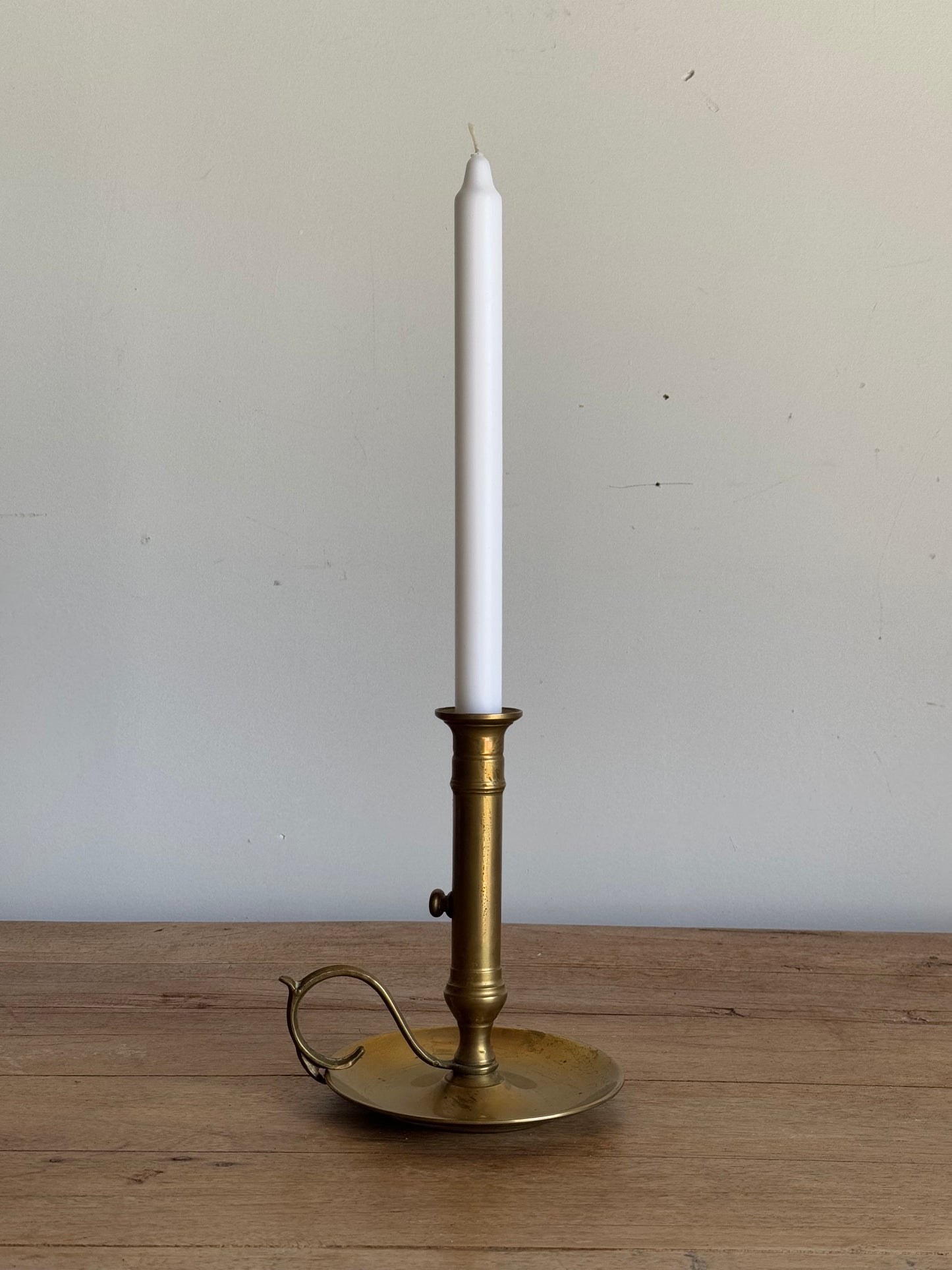 Brass candle holder with a white candle on a wooden surface and light gray background
