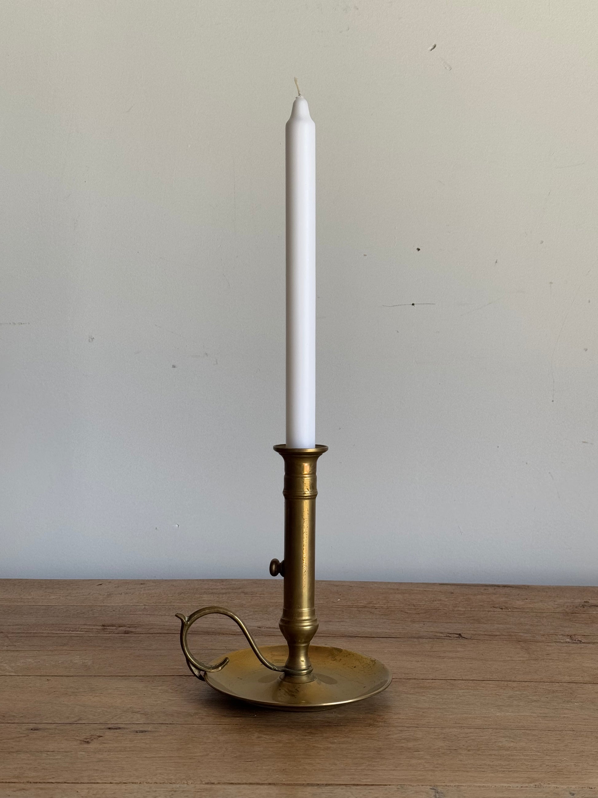 Brass candle holder with a white candle on a wooden surface and light gray background