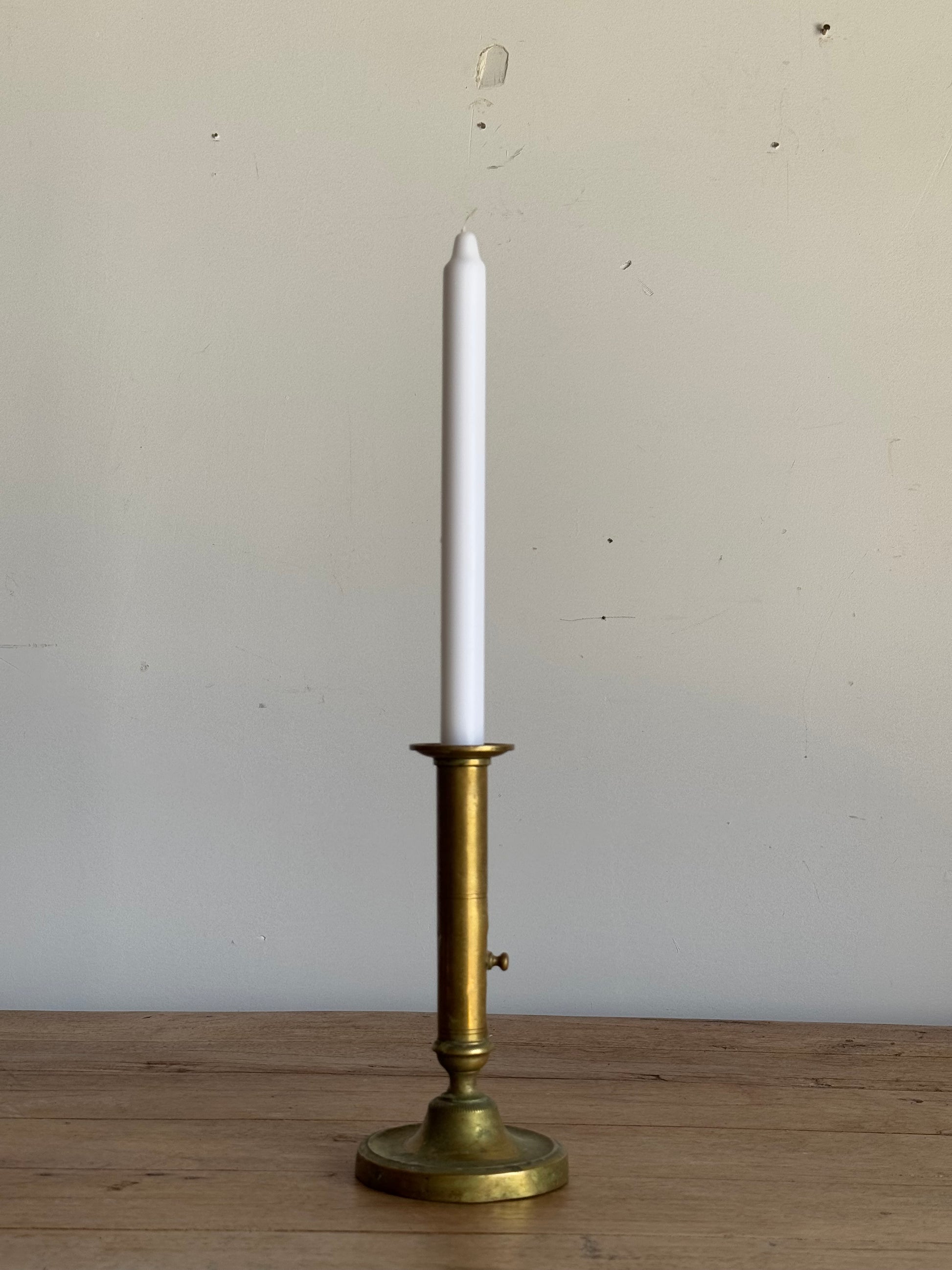 White candle in a brass candlestick holder against a neutral background