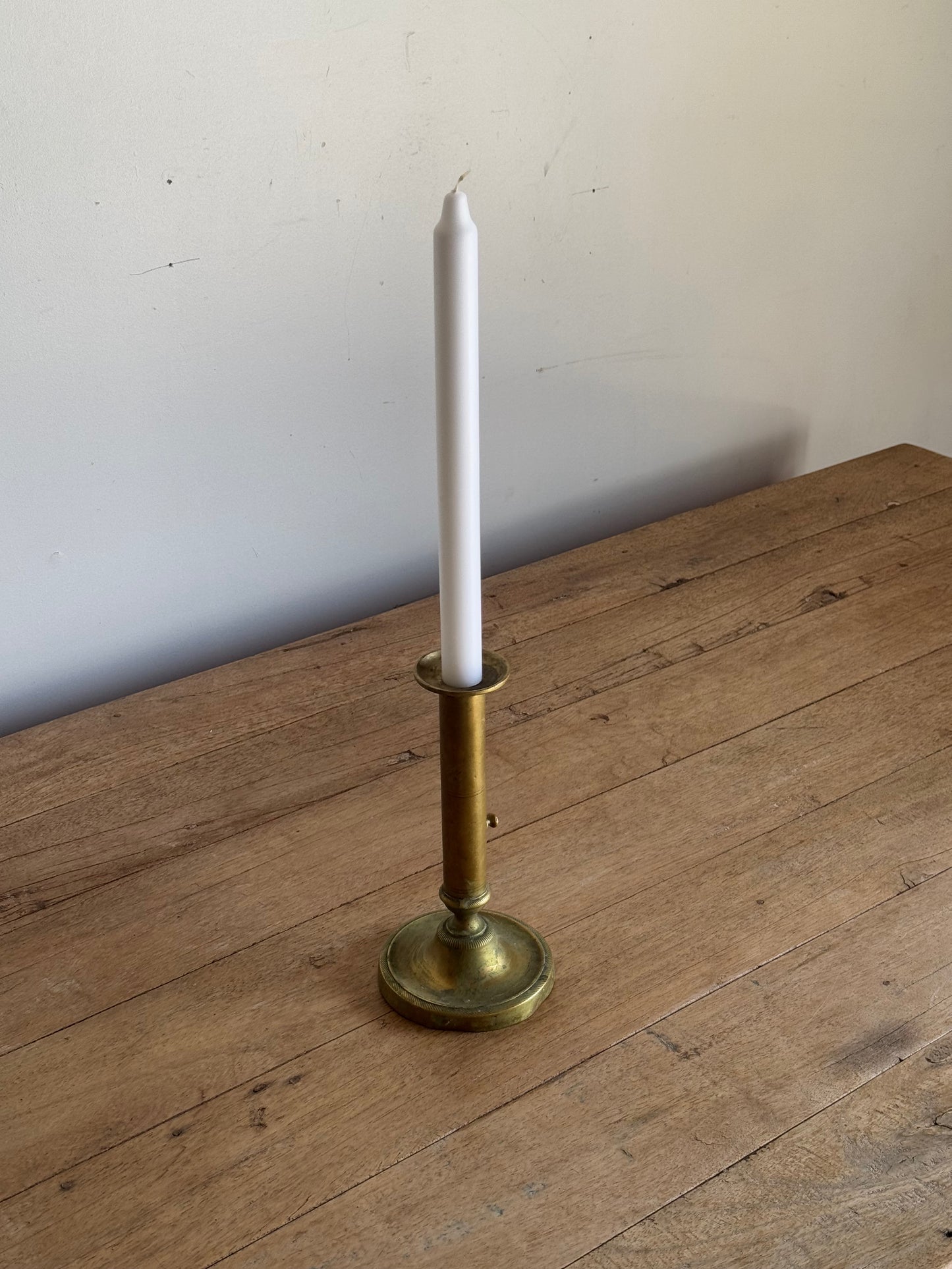 brass candle holder with a white candle on a wooden surface.