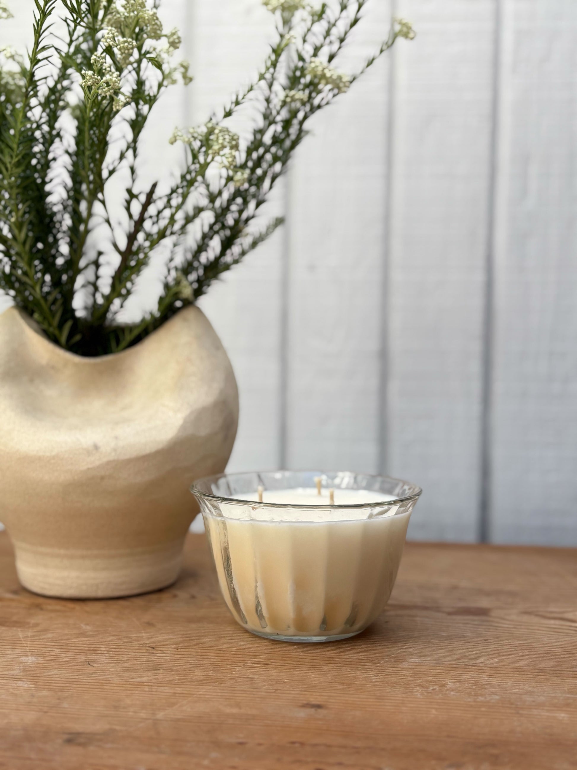 Glass candle with wooden base and vase with plants on a wooden surface