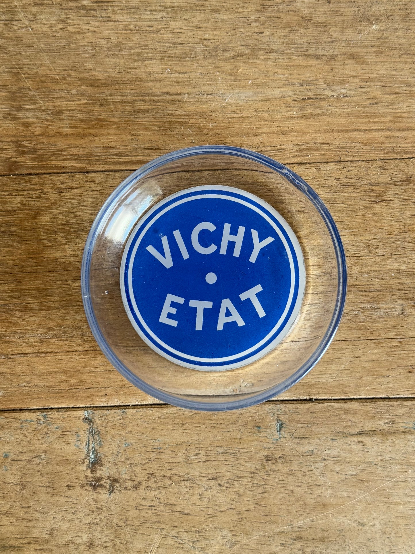Clear glass dish with blue circular logo on a wooden surface