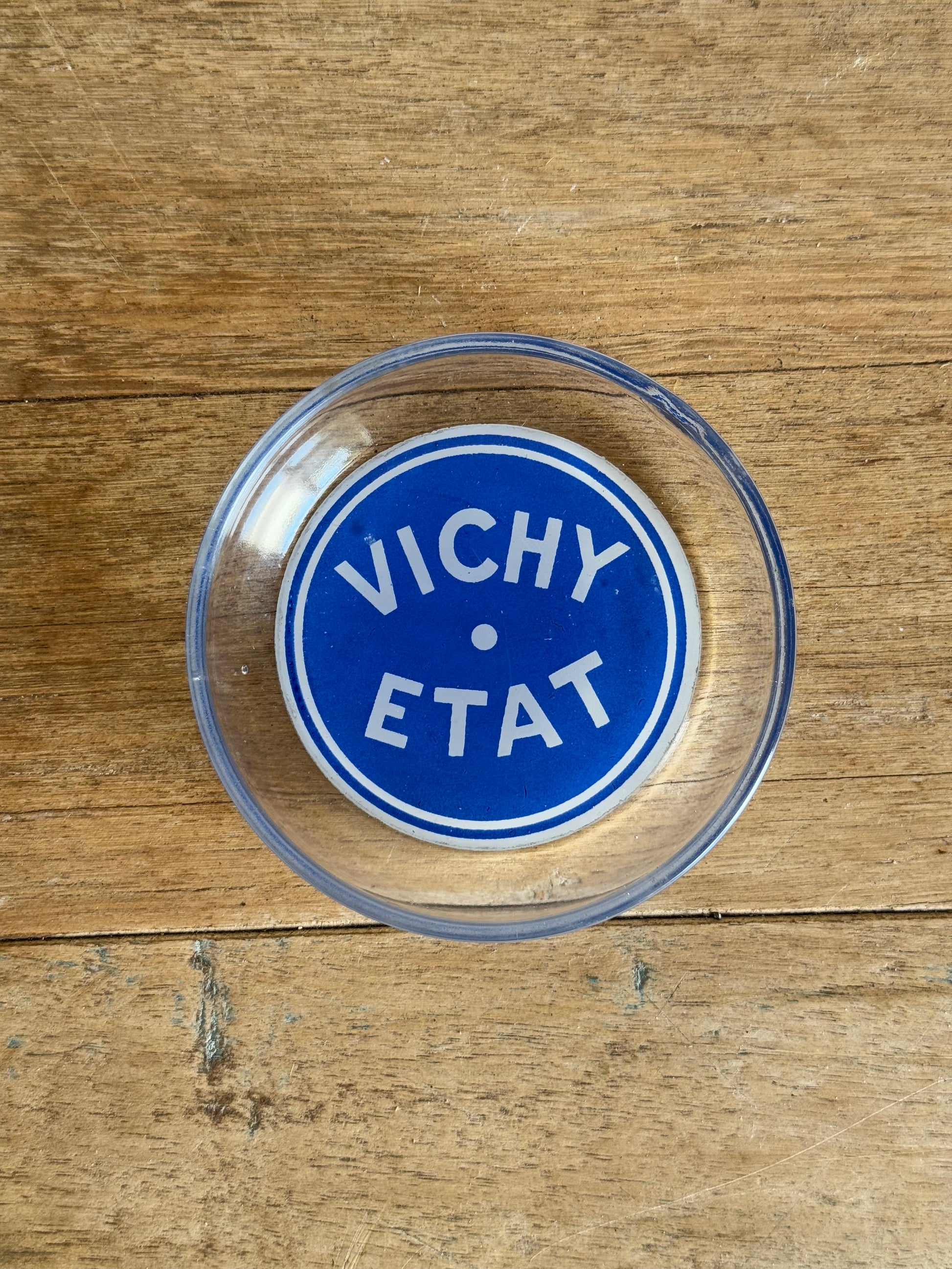 Clear glass dish with blue circular logo on a wooden surface