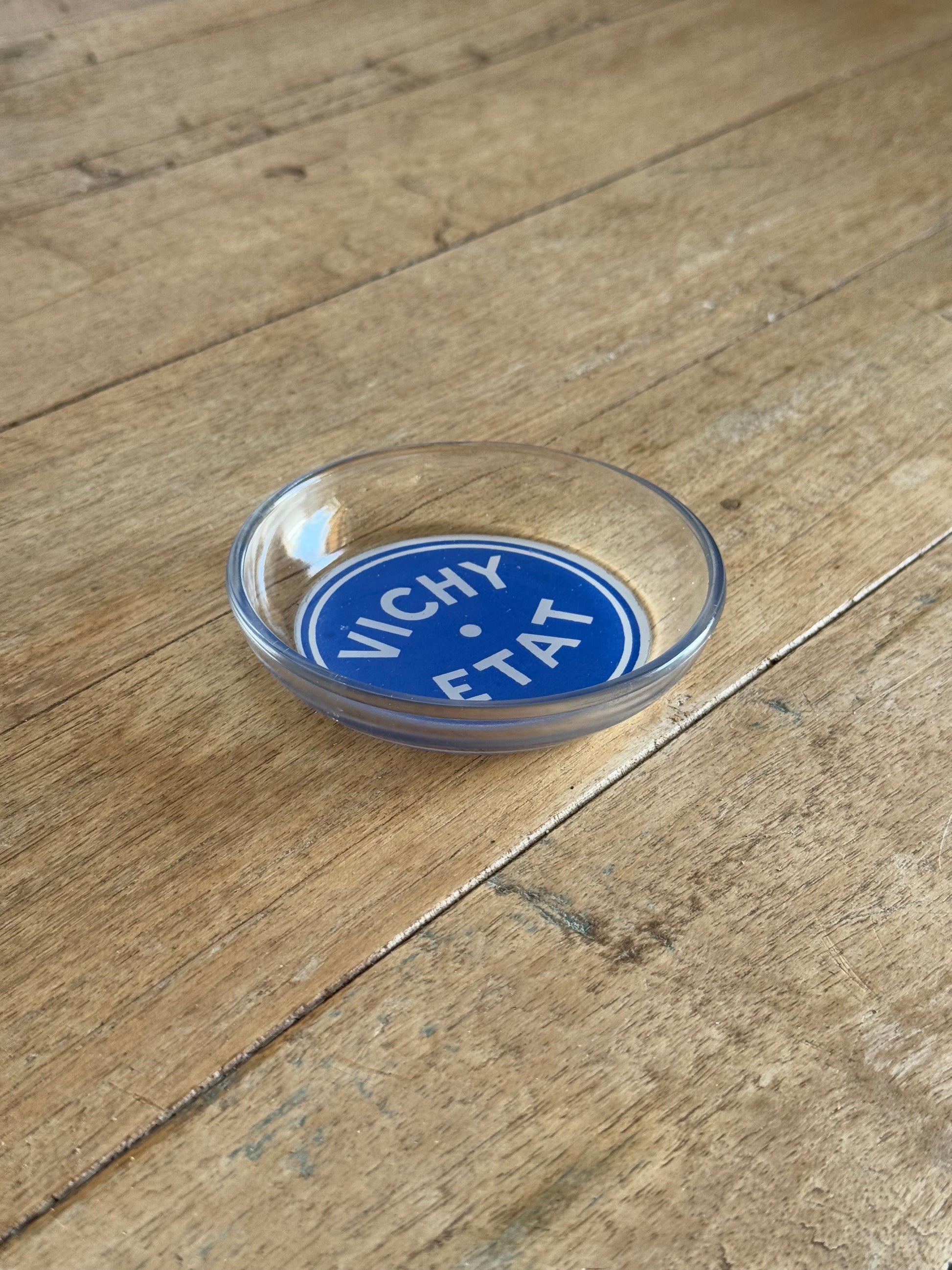 glass dish with Round blue label with 'Vichy' text on a wooden surface