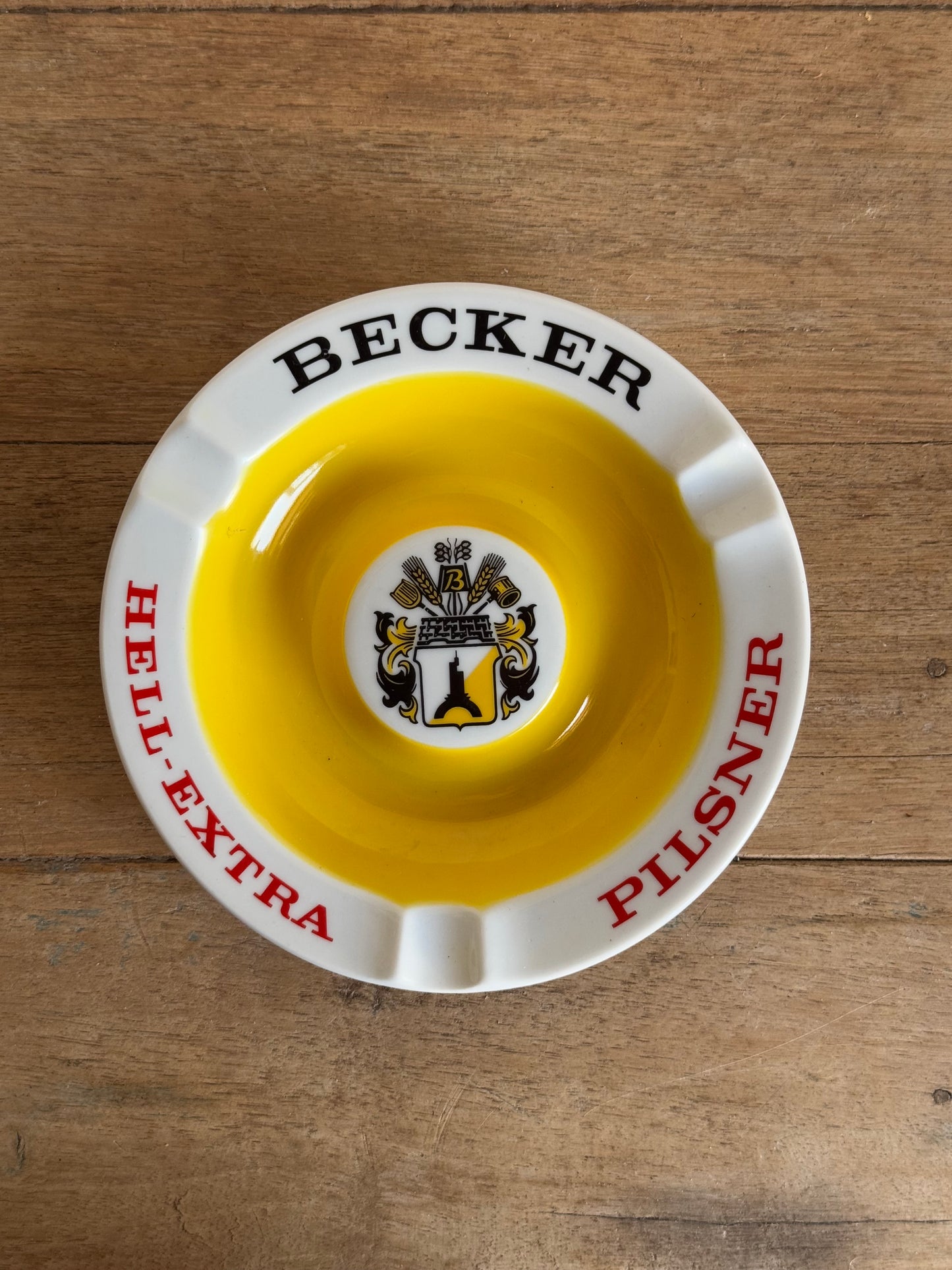 Vintage ashtray with 'Becker' and 'Pilsner' branding on a wooden surface