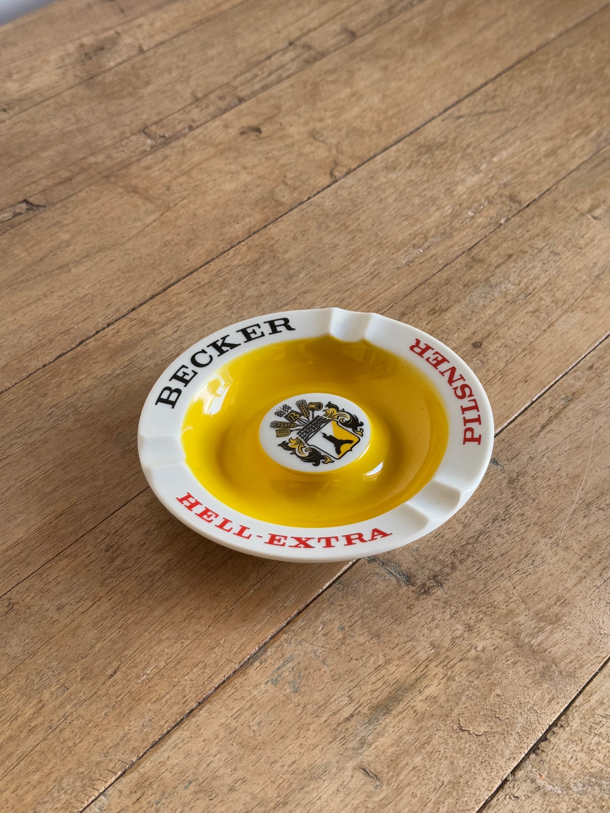 Ceramic ashtray with 'Becker' branding on a wooden surface