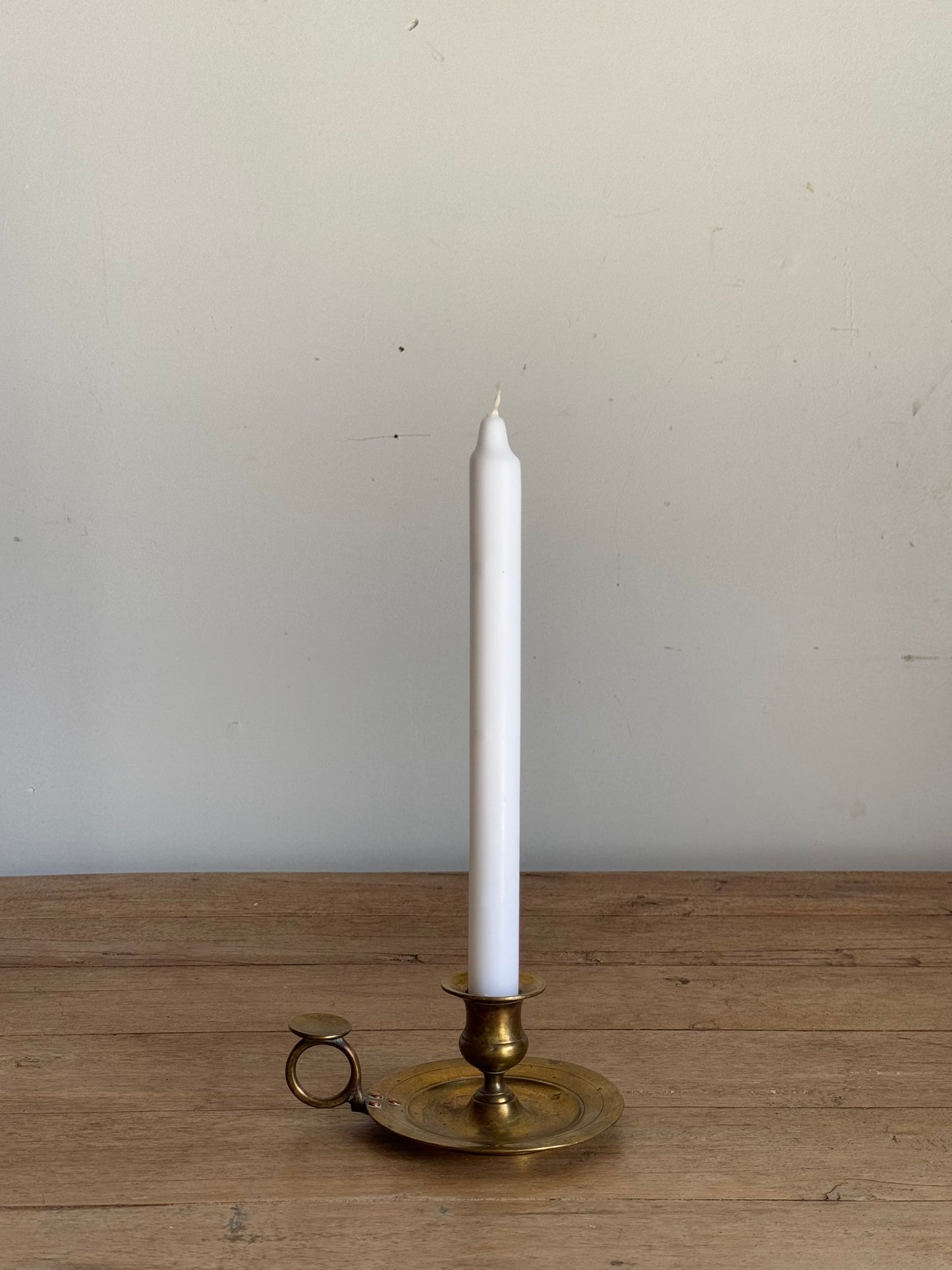 White candle in a brass candlestick holder on a wooden surface with a light gray background