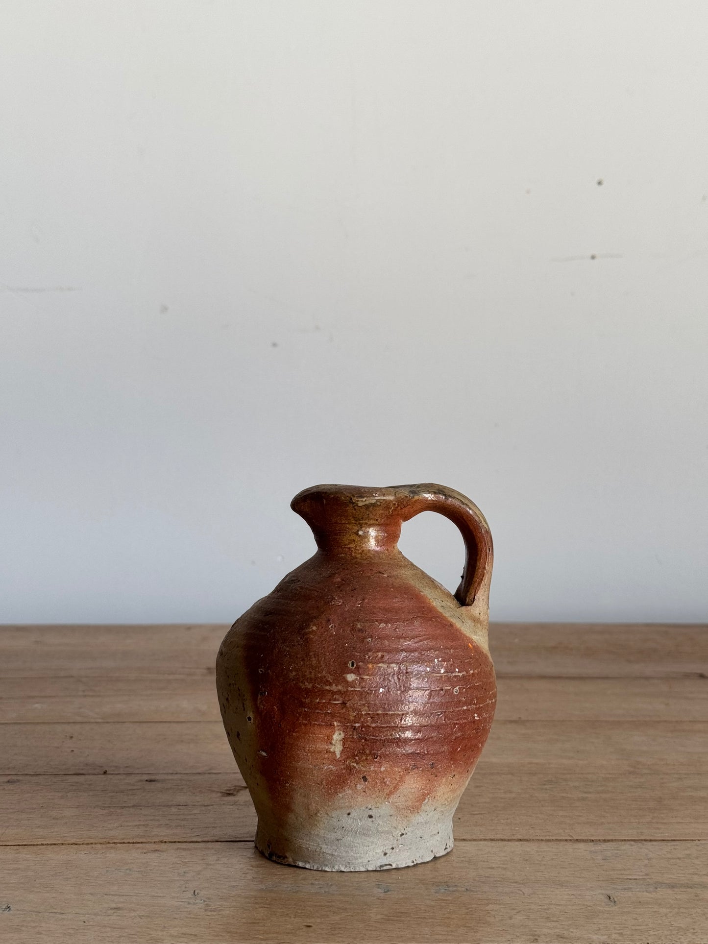 Small ceramic jar with a handle on a wooden surface