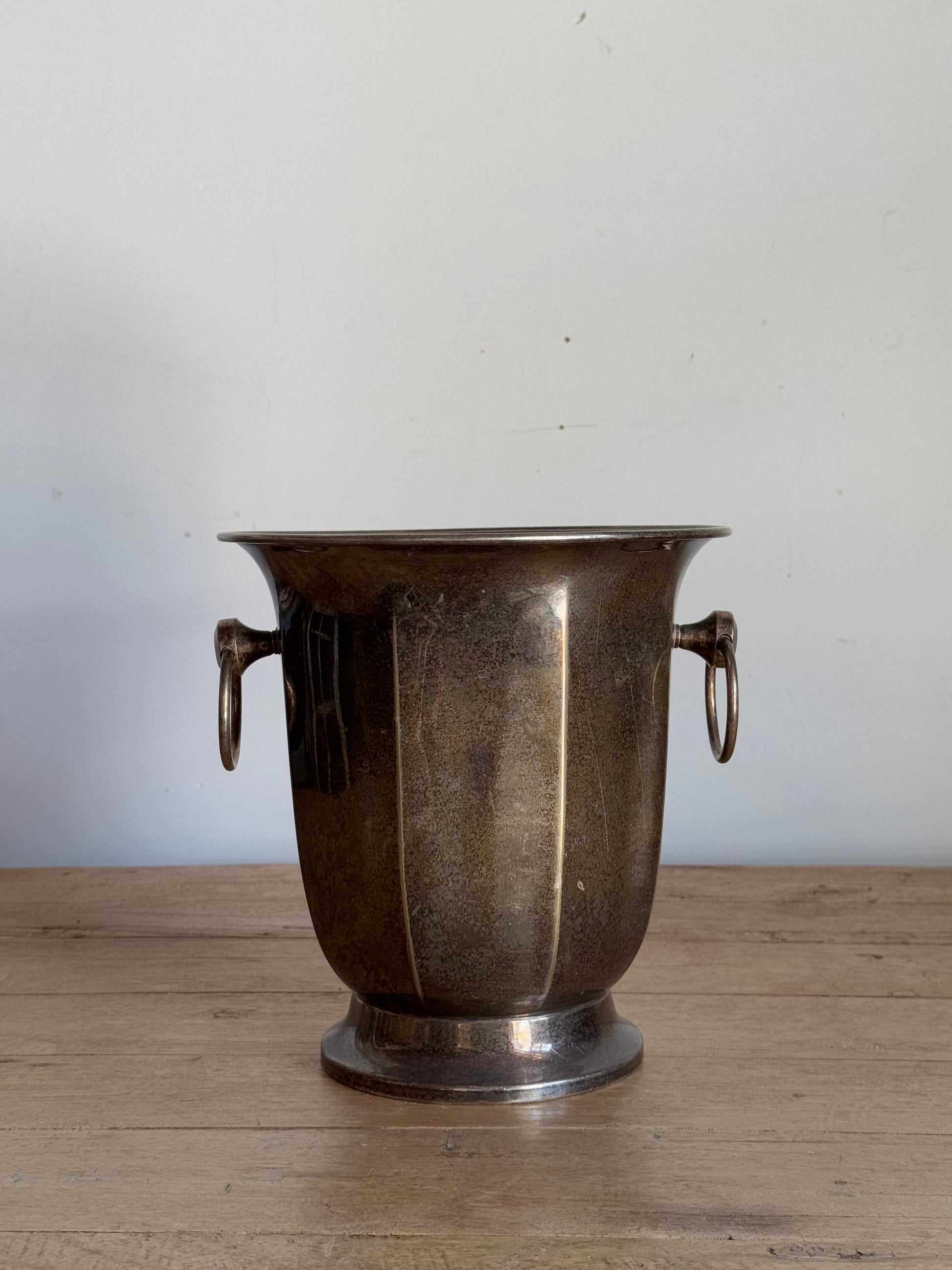 Bronze vase with handles on a wooden surface against a white wall