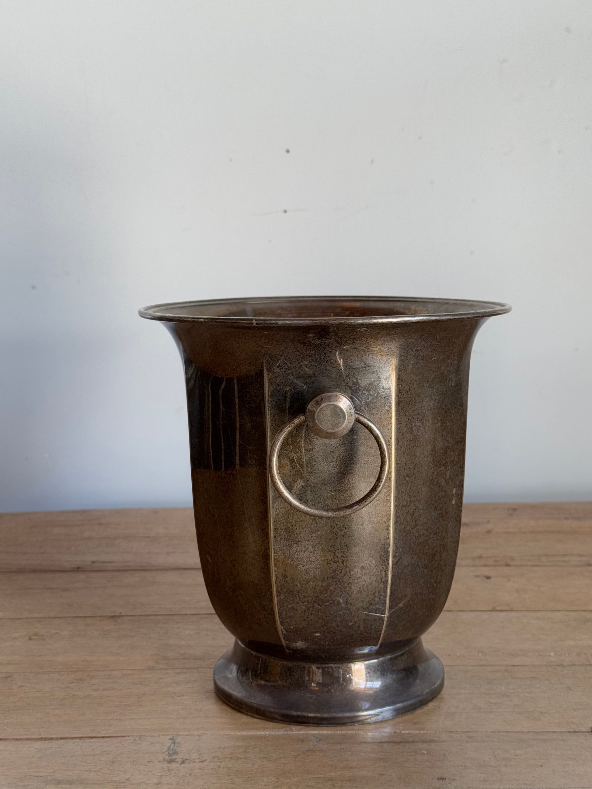 Vintage-style metal vase with a handle on a wooden surface and light gray background