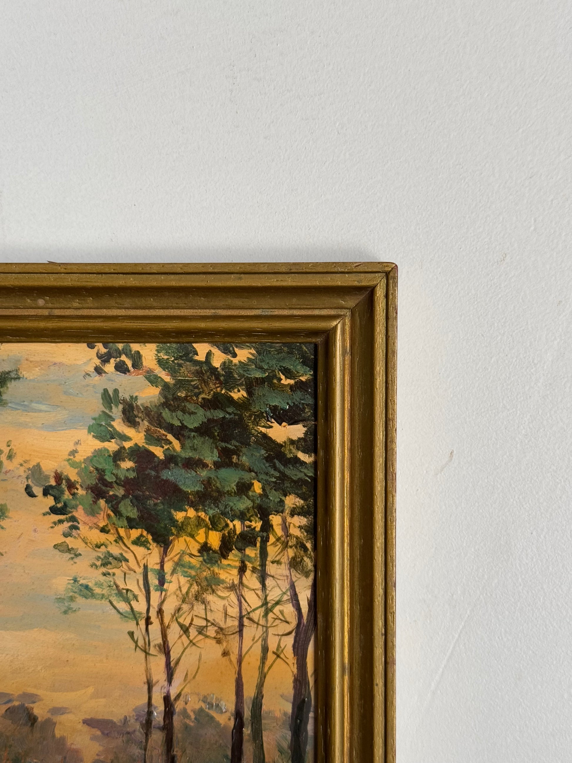 Framed painting of a landscape with trees on a light gray wall