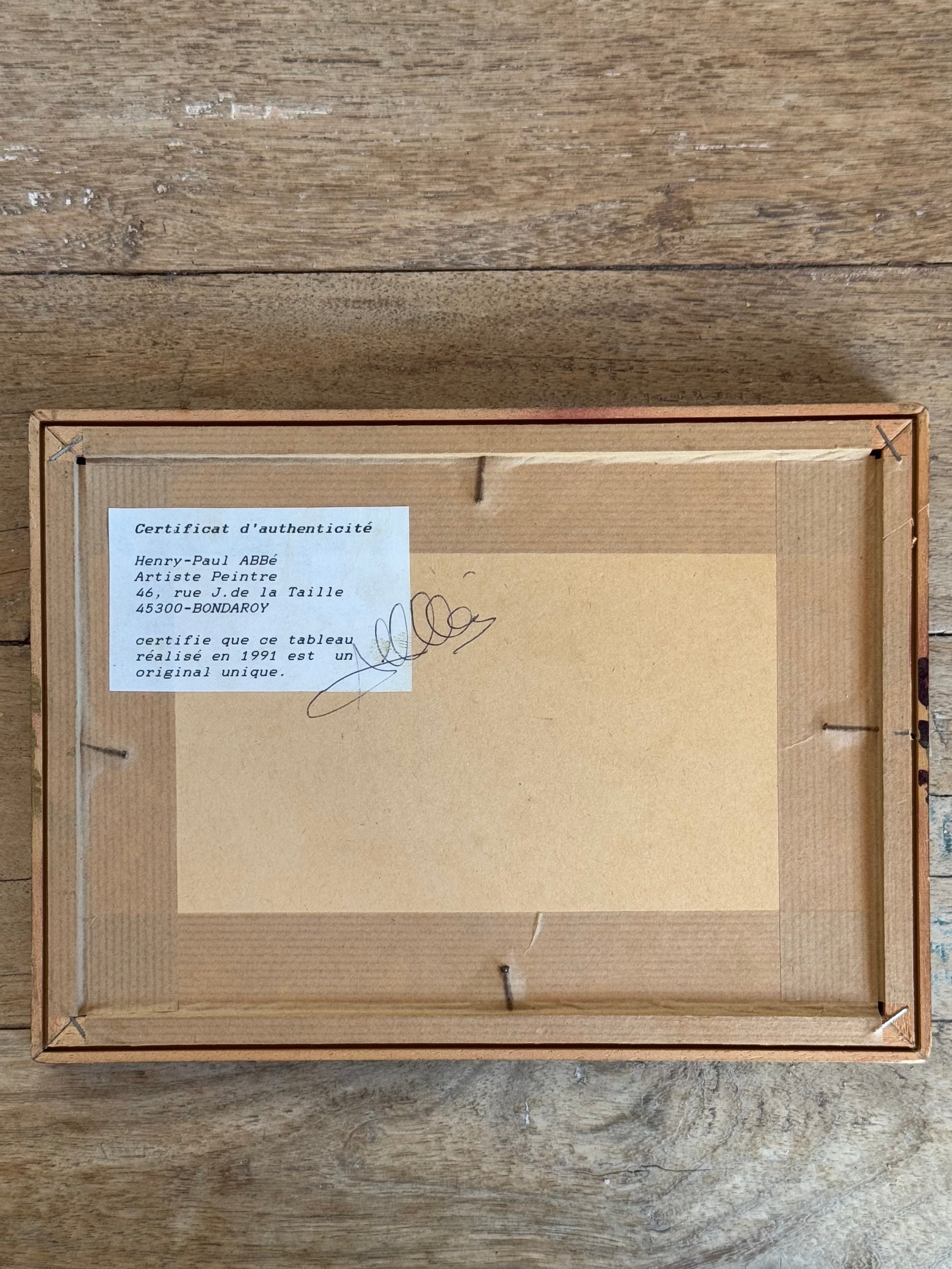 Framed artwork with a certificate of authenticity on a wooden surface