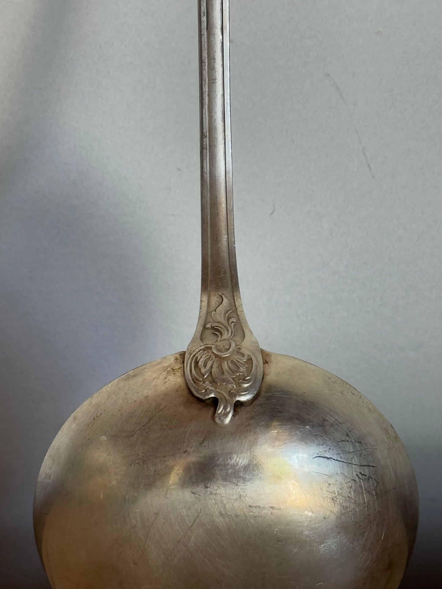 Silver ladle with ornate handle on a gray background
