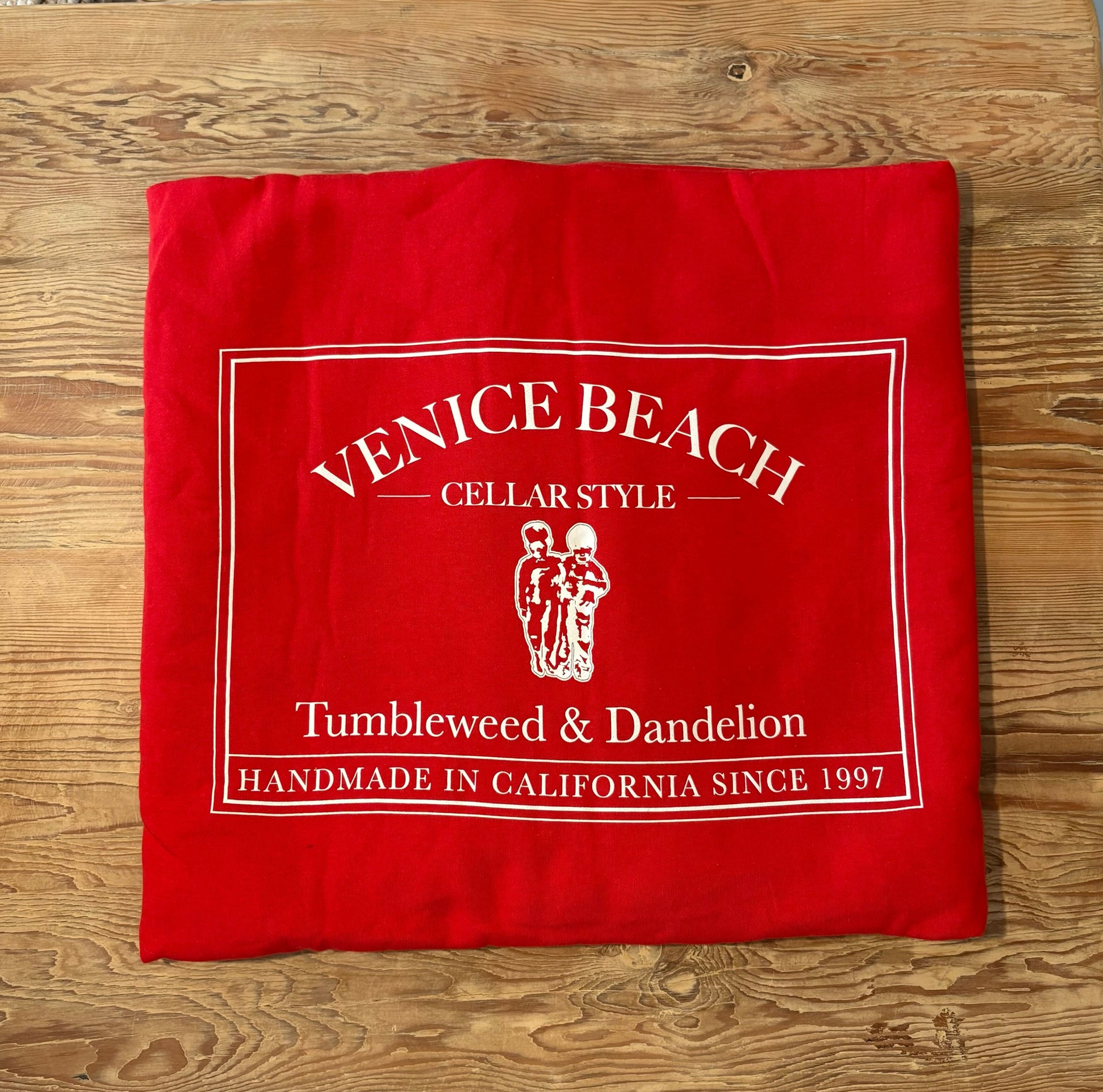 Red beach blanket with 'Venice Beach Cellar Style' branding on a wooden surface