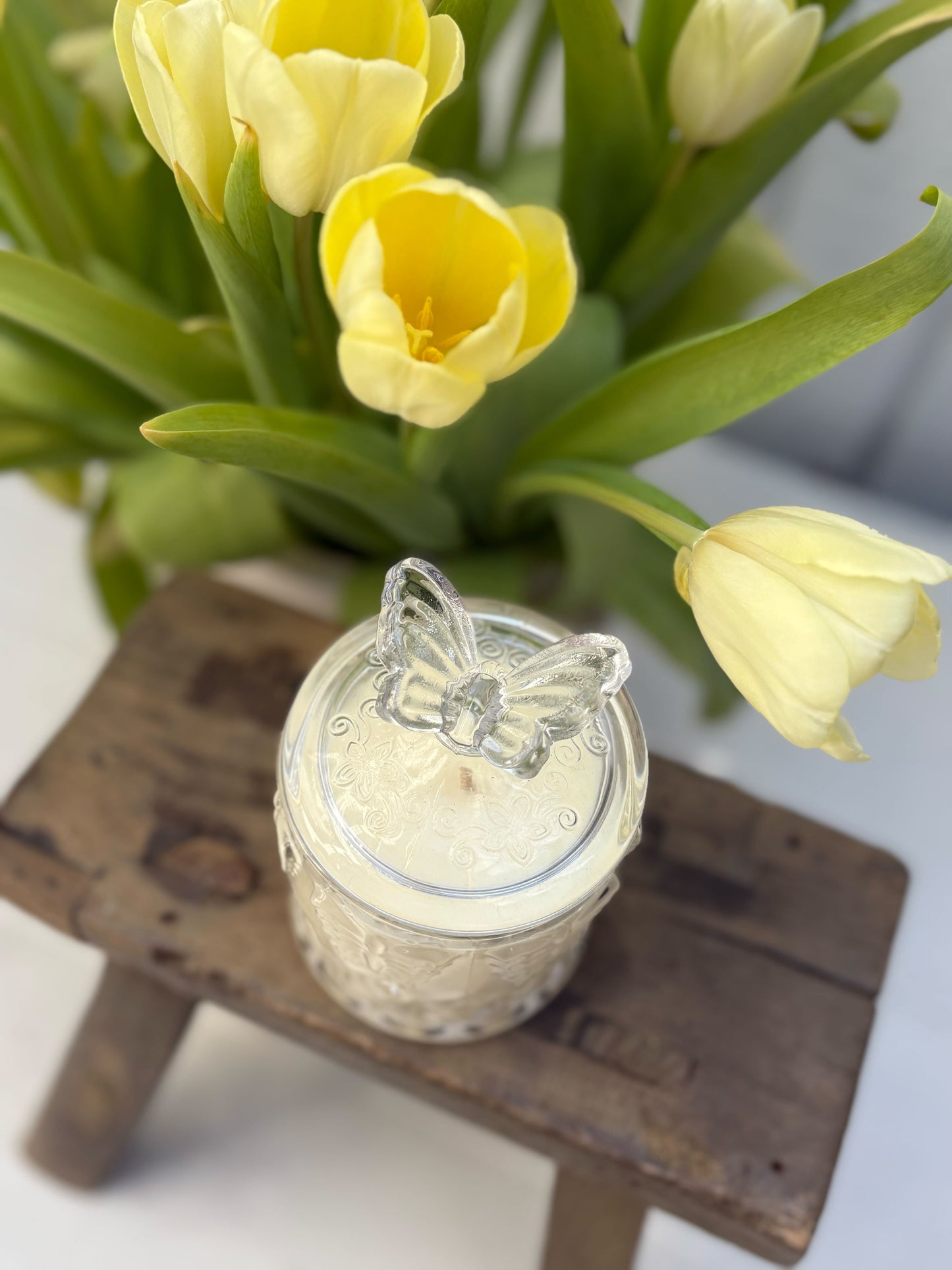 Jar of cream with butterfly lid on a wooden stool, yellow tulips in the background