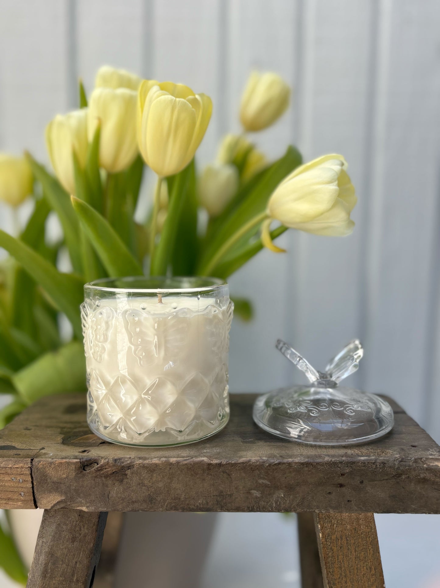 Glass candle holder with textured design on a wooden table with tulips in the background