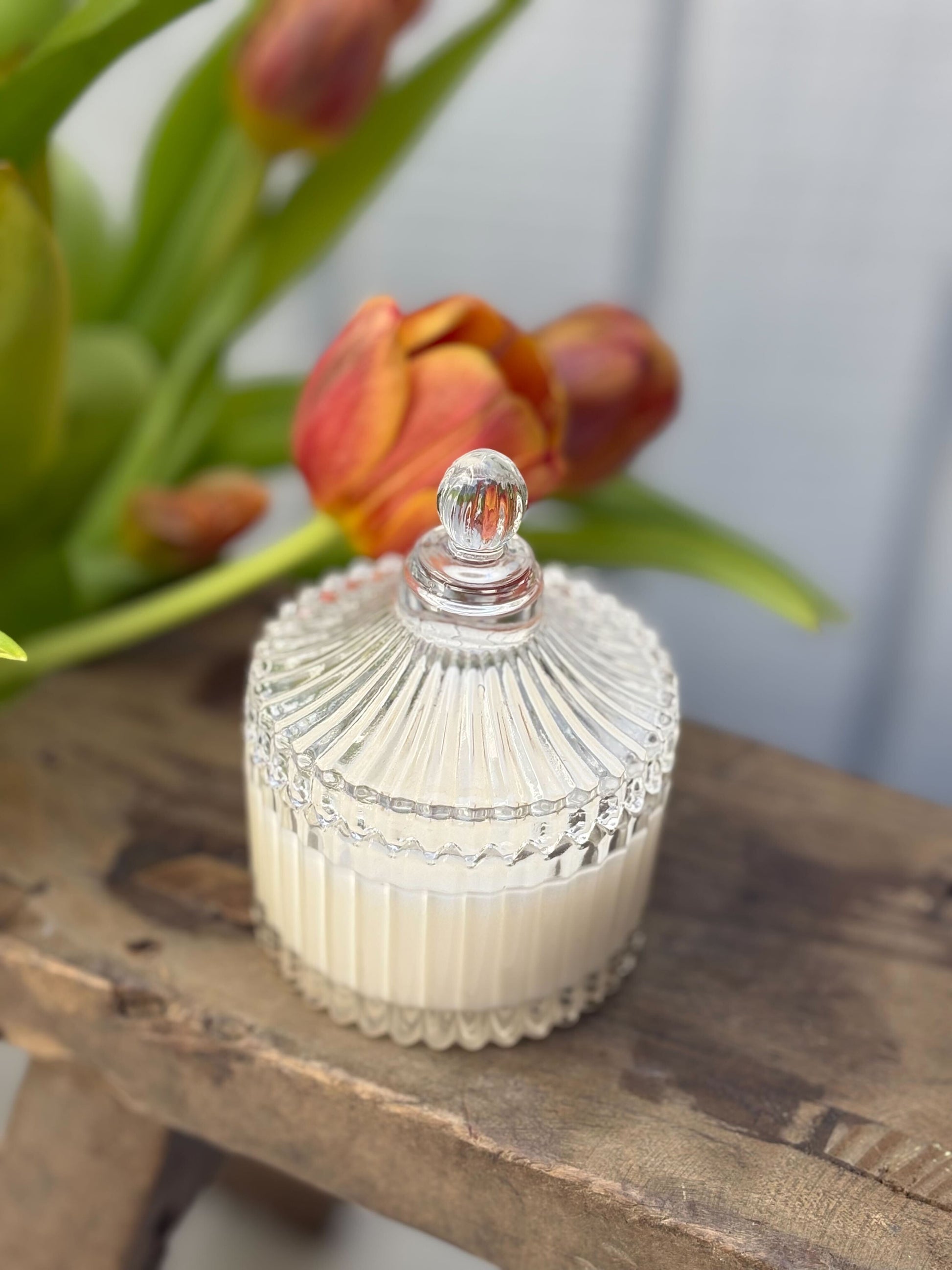 Decorative glass jar with a ribbed design on a wooden surface with flowers in the background