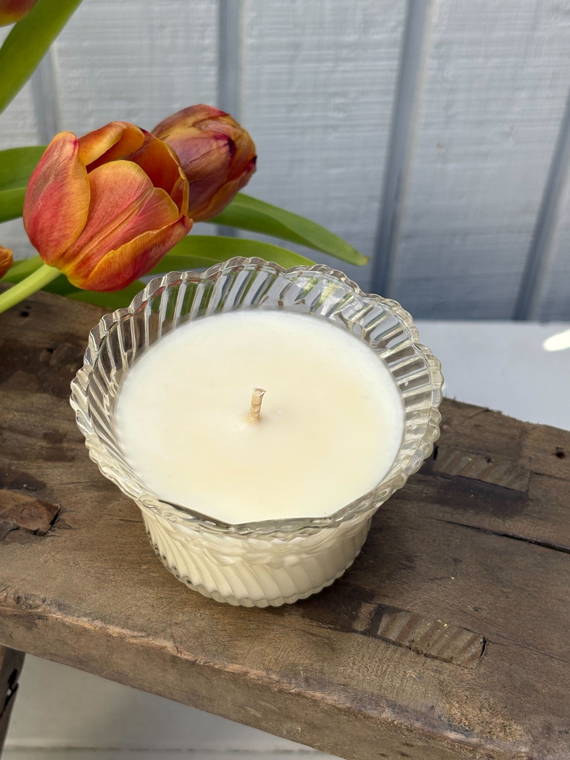 Candle in a textured glass holder with tulips on a wooden surface