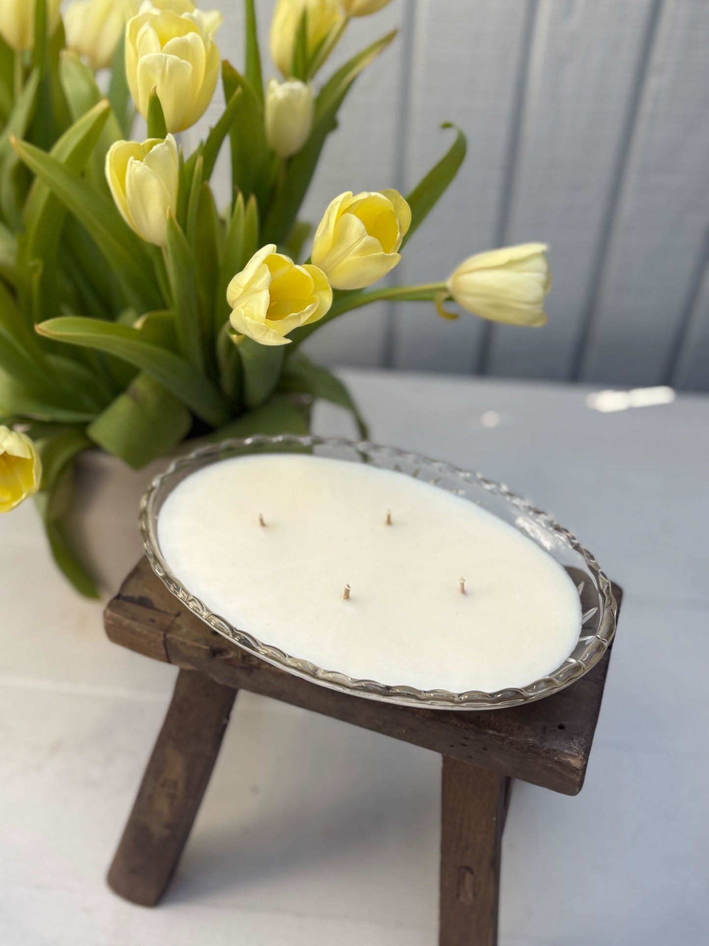 Candle on a small wooden stand with yellow tulips in the background