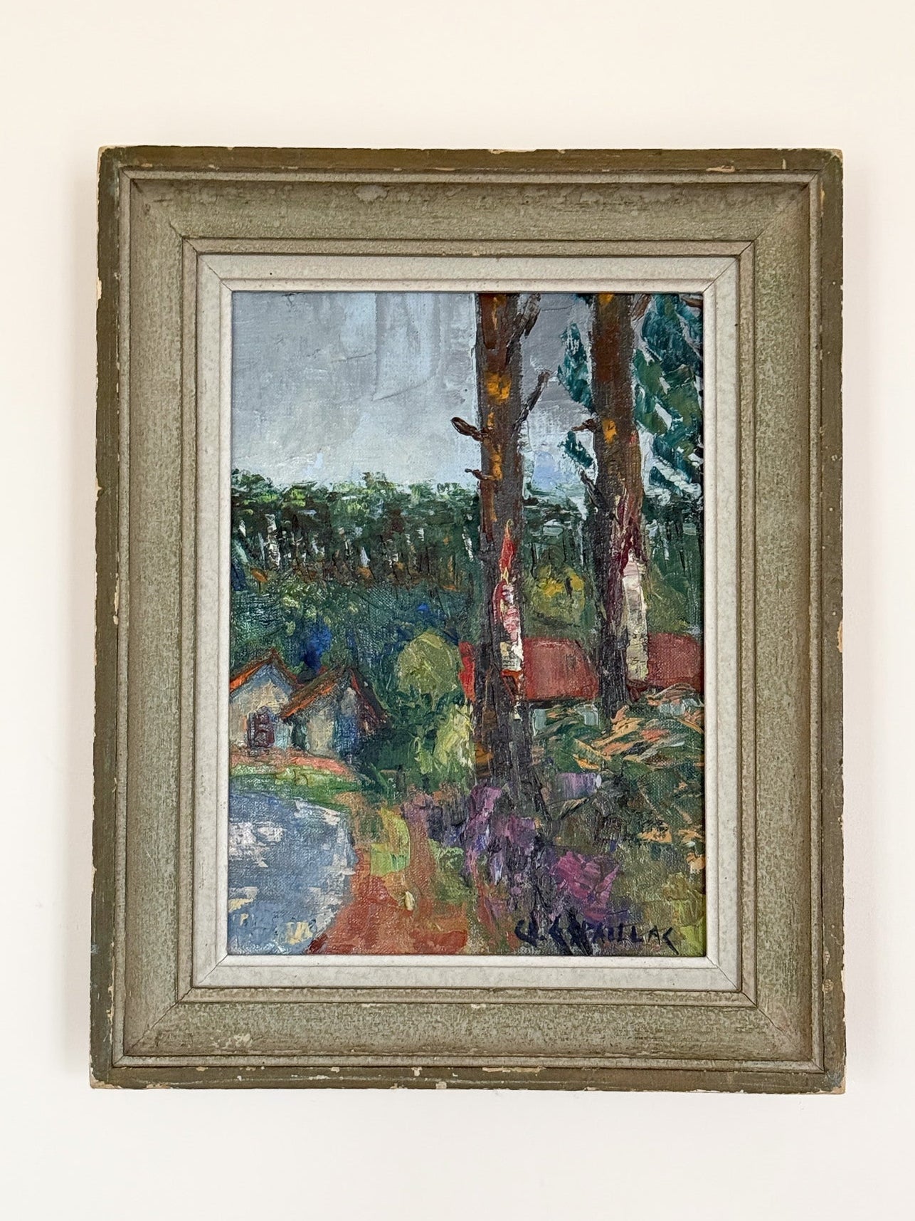 Framed painting of a landscape with trees and houses on a white wall