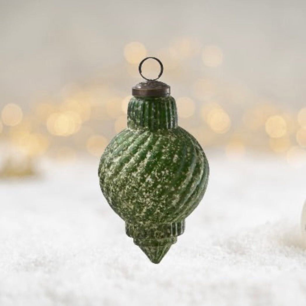 Green textured Christmas ornament on a snowy background with blurred lights