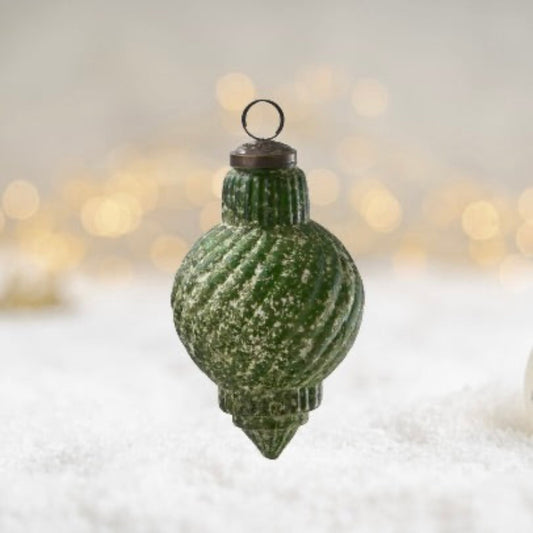 Green textured Christmas ornament on a snowy background with blurred lights