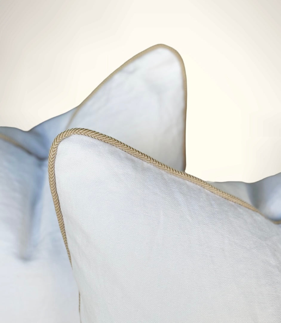 Close-up of a white pillow with beige piping on a light gray background