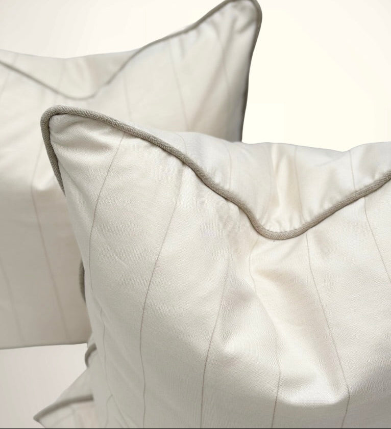 Close-up of two white pillows with gray piping on a light background