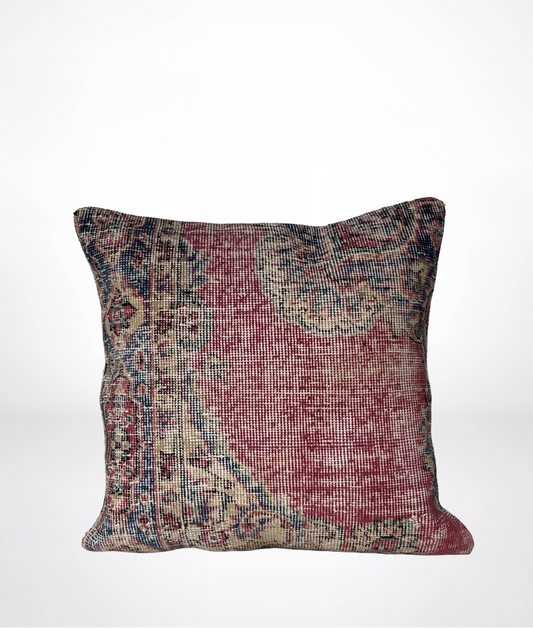 A square throw pillow featuring a distressed, vintage-style Persian or oriental rug pattern in muted red, beige, and blue tones, set against a plain white background.