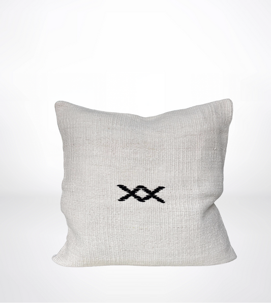 A square off-white linen throw pillow with a black embroidered double-X symbol in the center, set against a clean white background.
