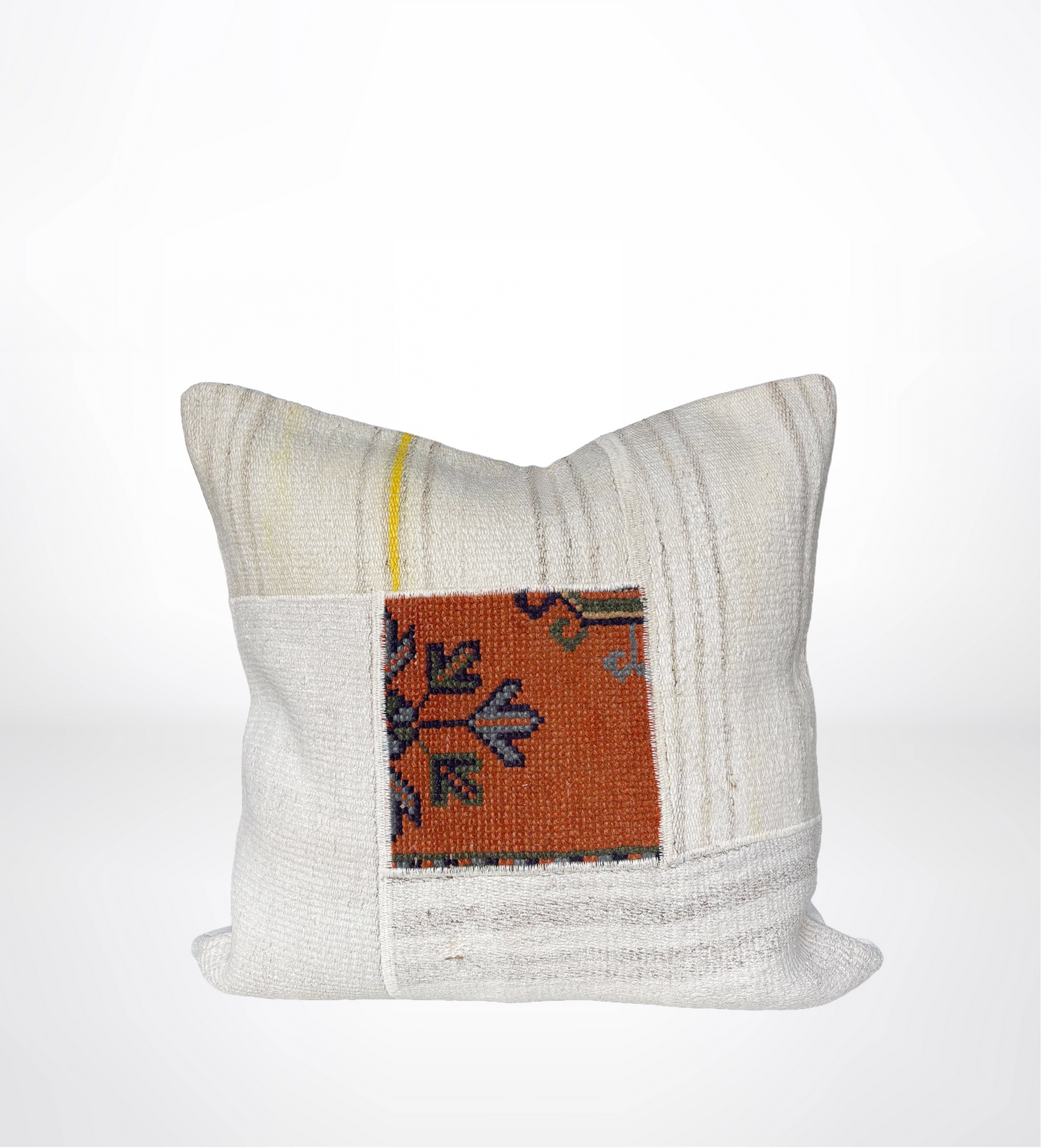 A square decorative throw pillow in off-white woven fabric with a central patch featuring an orange, blue, and gray patterned textile design.