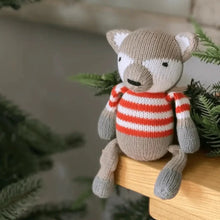 Load image into Gallery viewer, Knitted fox toy wearing a striped sweater on a wooden surface with greenery in the background