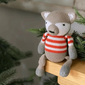 Knitted fox toy wearing a striped sweater on a wooden surface with greenery in the background