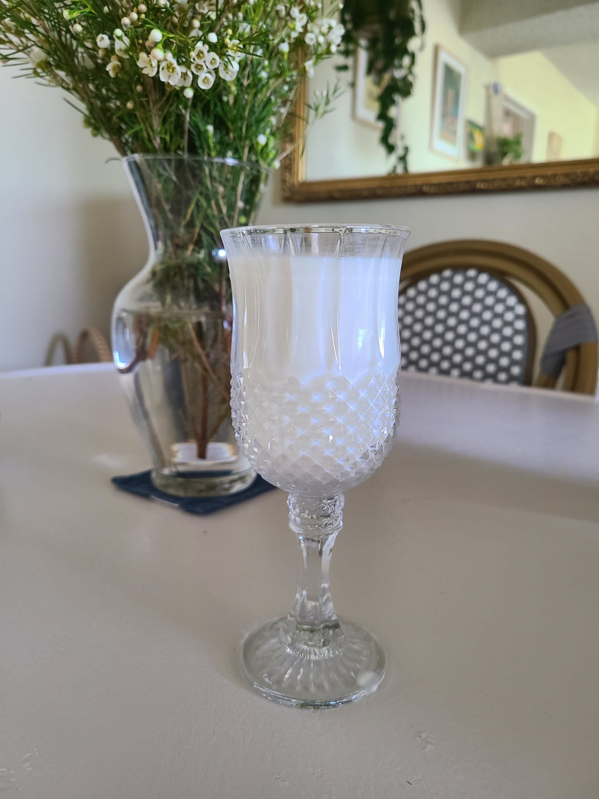 Clear glass candle holder with white candle on a surface, with a blurred background