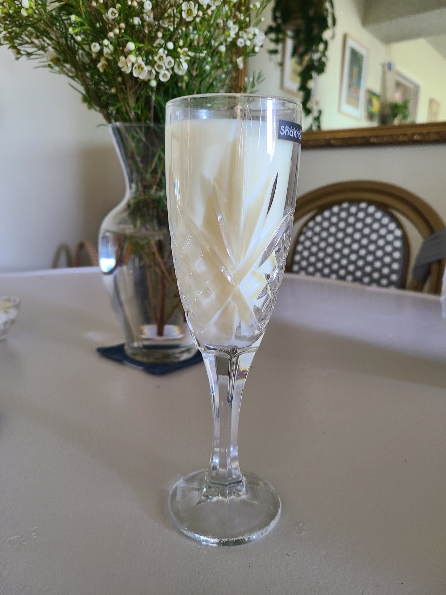 Clear glass with white floral design with white candle in it on a reflective surface