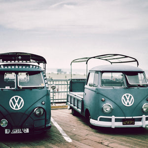photo of two green vintage VW vans in parking lot at the beach