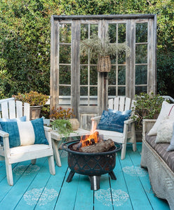 patio with turquoise painted wood deck with white medallions, white wood patio chairs with blue pillows, vintage wicker sofa, fire pit and large upright old windows as backdrop