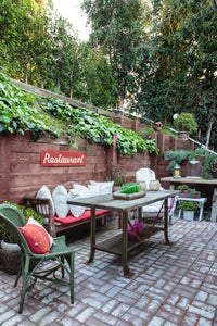 brick floor outdoor living space with vintage furniture, red and white pillows and red sign that says "restaurant" hanging on wooden hill support