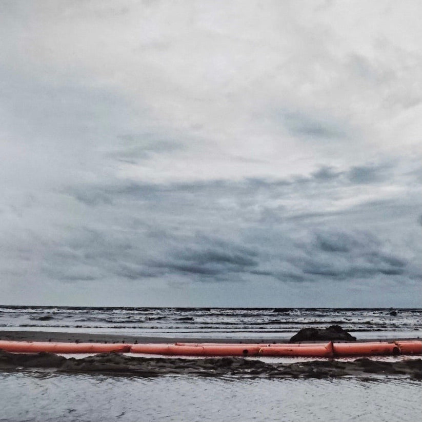 ocean with gray clouds and red barrier at shore line