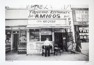 black and white photo of front of an old taqueria with man standing in front  Edit alt text