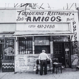 black and white photo of front of an old taqueria with man standing in front