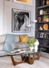 Load image into Gallery viewer, area of a living room with gray sofa, wood and glass coffee table with white vases, a large black and white framed photo of a stone statue, part of built-in shelves with miscellaneous decorative items on shelves