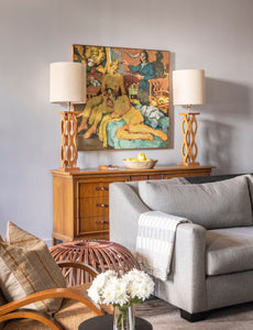 part of a living room, with gray sofa, caramel colored wood credenza, two lamps, colorful painting on wall