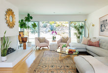 Load image into Gallery viewer, photo of a living room with white sofa, area colored upholstered chairs, gold mirror above fireplace, a conga drum and houseplants