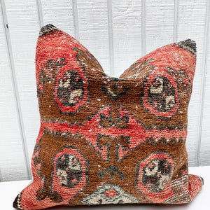 square pillow made from a Turkish rug with salmon red and brown colors