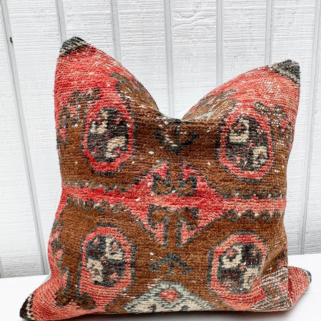 square pillow made from a Turkish rug with salmon red and brown colors