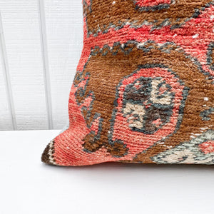 square pillow made from a Turkish rug with salmon red and brown colors