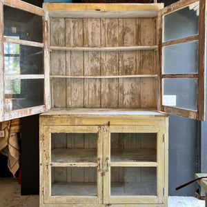 rustic hutch of old wood with distressed butter yellow paint finish, glass doors on top and  bottom