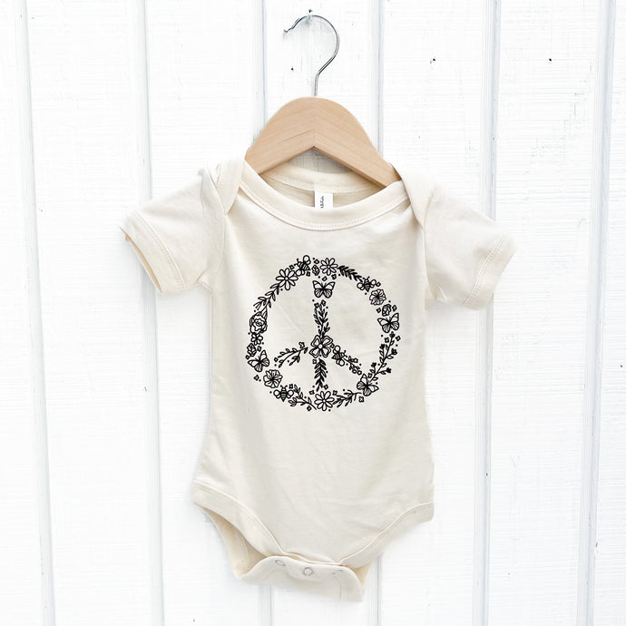 off white short sleeved baby onesie with black peace sign flower wreath on front